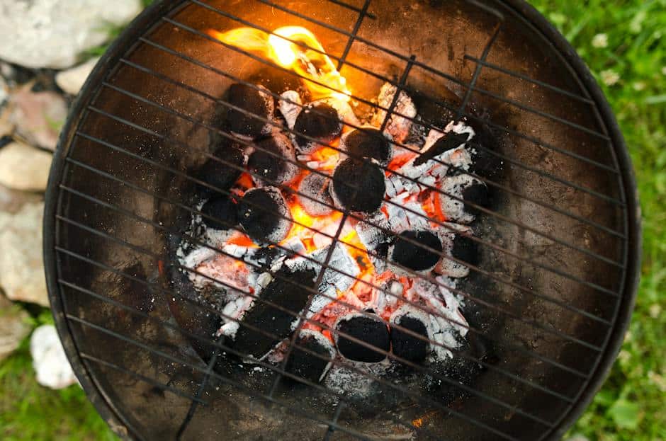 A close-up image of a charcoal grill with smoke rising from it and a perfectly seared steak on the grate.
