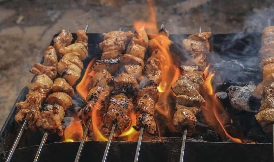 An image showing delicious grilled meat and vegetables on a grill with flames in the background.