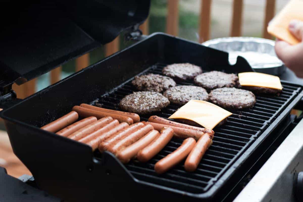 An image representing tailgating safety. It shows a person grilling with a safe distance maintained from vehicles and people. They are wearing protective gloves and an apron. The wind is blowing in the opposite direction of the grill. The image symbolizes responsible grilling practices.